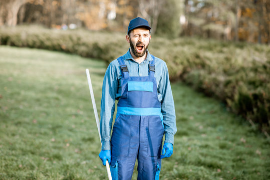 Funny portrait of a professional sweeper in uniform yawning during the work in the garden