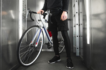 Sports young man stands with a bicycle in the elevator. Close-up photo of foot and bike.