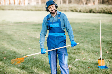 Professional male sweeper or gardener in uniform listening to the music with headphones while...
