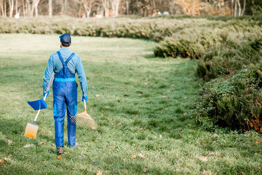 Professional sweeper or gardener in working uniform walking with cleaning tools in the garden