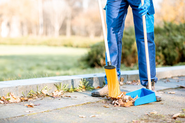 Man sweeping leaves with orange broom to the scoop on the street, close-up view with no face