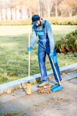 Professional sweeper in uniform sweeping leaves with broom and scoop on the street