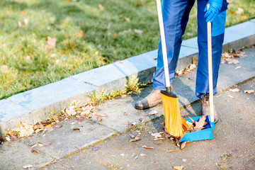 Man sweeping leaves with orange broom to the scoop on the street, close-up view with no face