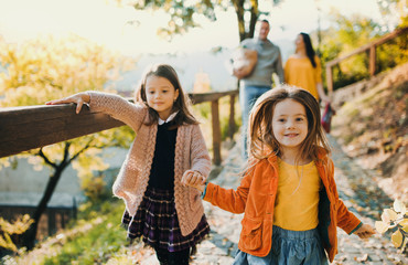 Two girls with unrecognizable parents in the background walking in park in autumn.