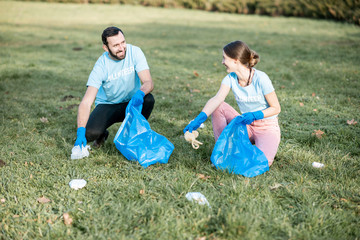 Happy man and woman volunteers dressed in blue t-shirts cleaning public garden from plastic rubbish...