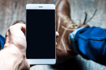 A young man takes pictures of his shoes on a mobile phone. Point of view