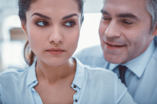 Vulgar whisper. Unpleasant man whispering in ear of his scared good-looking female coworker