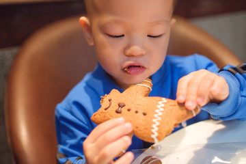 Cute little Asian 2 years old toddler baby boy child eating Gingerbread Man - Christmas symbol, Children eat ginger man. Waiting for Christmas. Celebration. New Year concept. . .......
