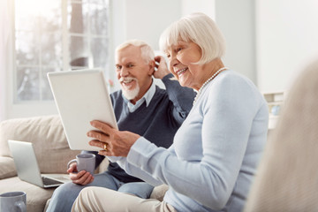 Fototapeta premium Positive vibes. Cheerful couple of baby boomers looking through the photos on the tablet while having a good weekend