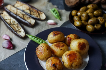 Delicious dinner table for two with fried potatoes, olives,  eggplants and green peas on dark stone background.