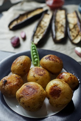 Delicious dinner table for two with fried potatoes, eggplants and green peas on dark stone background.