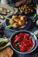 Delicious dinner table for two with fried potatoes, organic tomatoes salad, olives, green onion, eggplants on dark stone background.