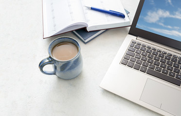 Obraz na płótnie Canvas laptop, calendar and a blue cup of coffee on a bright desk, copy space