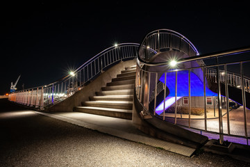 Colorful illuminated walkway inHarlingen with strap and metal silver balustrade in an organic curve shape.