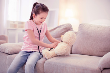 Play with bear. Cute little girl pretending to be a doctor playing with her teddy bear in the living room