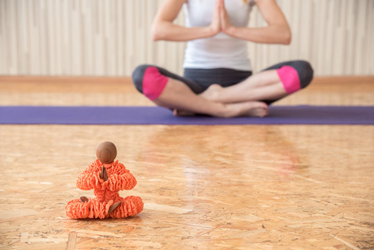 A girl practices yoga in a gym and sits in a lotus position with a puppet doll