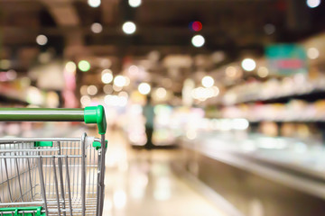 Empty green shopping cart with abstract supermarket grocery store blurred defocused background with...