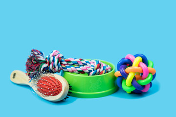 Pet accessories concept.  Brush, rubber toy and rope in bowls for pet on color background