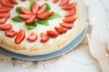 Very beautiful summer cheesecake decorated with strawberries - stands on a white wooden table, close-up.