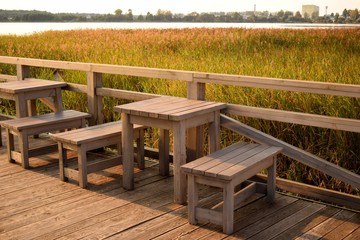 Wooden tables and benches on the lake with reeds waiting for lovers to watch the sunset.