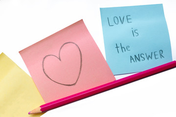 love is the answer - handwritten title on the blue sticker, heart drawing on a pink paper and a pencil. Saint Valentine's Day conceptual cards on the white background