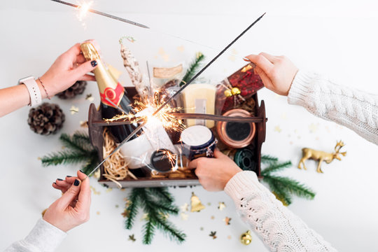 Unrecognizable Women Holding Sparklers And Opening Wooden Basket With Food For Christmas Selebration. Happy Winter Holidays. Presents For Christmastime.