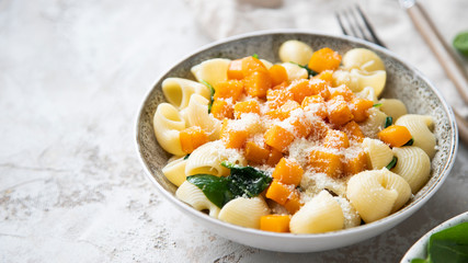 Pasta with pumpkin, spinach and cheese on shabby grey background.