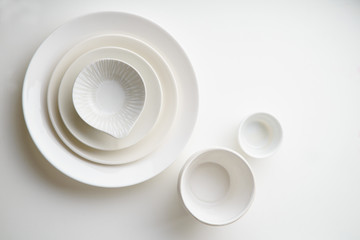 Porcelain plates of various form and size on white background. Overhead image, copy space.