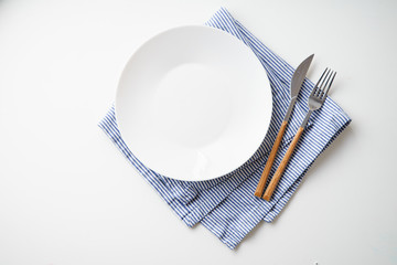 White empty plate with knife and fork on striped blue and white textile napkin on white background