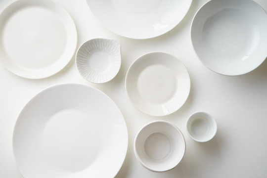 Porcelain plates of various form and size on white background. Overhead image, copy space.