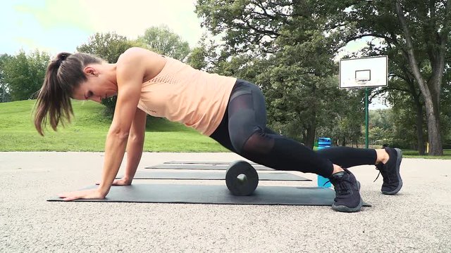 beautiful well-trained woman is doing exercises with the fascia roll, outdoor in the morning