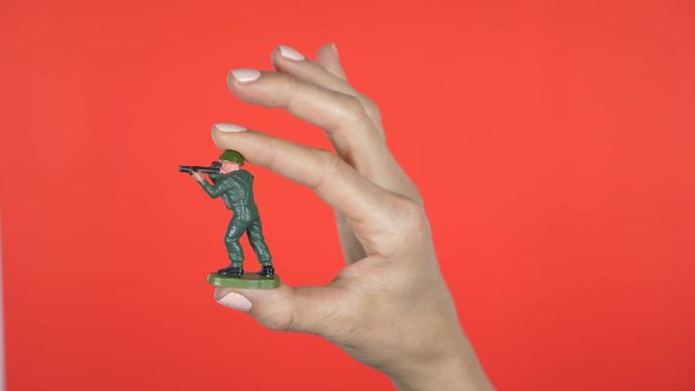 Closeup of female hand bringing green plastic toy soldier into frame.