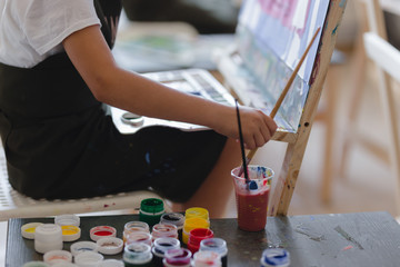 Little girl painting a picture in a studio or art school. Creative pensive painter child paints a colorful picture on canvas in workshop.