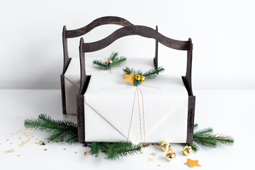 Luxury New Year gift with gold decoration and tree branches. Christmas gift in wooden basket. Christmas background with gift box. Presents for Christmastime celebration.