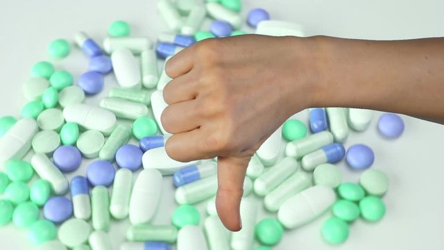 Female hand goes from thumbs up to thumbs down. Medical pill background. Note that thumb was shot against green screen and background has been keyed out to show rotating pills.