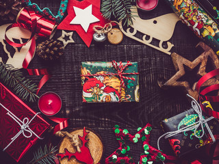 Fototapeta premium Box with gifts, colorful decorations, Christmas tree branches, candles and cones on a wooden, brown surface. Top view, close-up, flat lay. Greeting card. Merry Christmas and Happy New Year