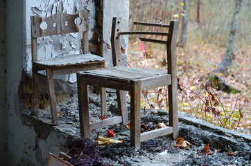 Small wooden chairs by window without glass in kindergarten against background of forest overgrown street, Pripyat, Chernobyl exclusion zone, Ukraine