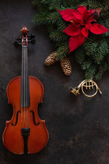 Fototapeta na wymiar Old violin and fir-tree branches with Christmas decor and poinsettia. Christmas and New Year's concept. Top view, close-up on dark concrete background.