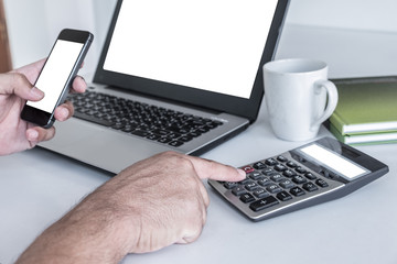 Men's hands are pressing the cell phone. And have a laptop white screen. calculator white screen a pencil is placed on a notebook. on the white desk.