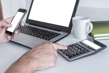 Men's hands are pressing the cell phone. And have a laptop white screen. calculator white screen a pencil is placed on a notebook. on the white desk.