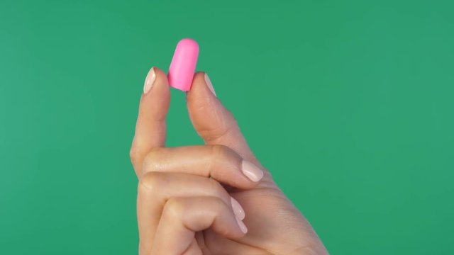 Female hand holds up pink ear plug for hearing protection. Green screen background.