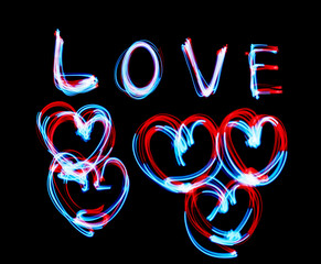 Glowing inscription LOVE on a black background. blue light image, long exposure with colored fairy lights, against black