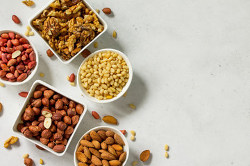 Various nuts in a ceramic bowl (walnut, almonds, pine nuts, hazelnuts) on a light stone table. The concept of a healthy dessert. Copy space.