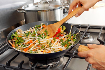 WOMAN IN KITCHEN STIR FRYING VEGETABLES