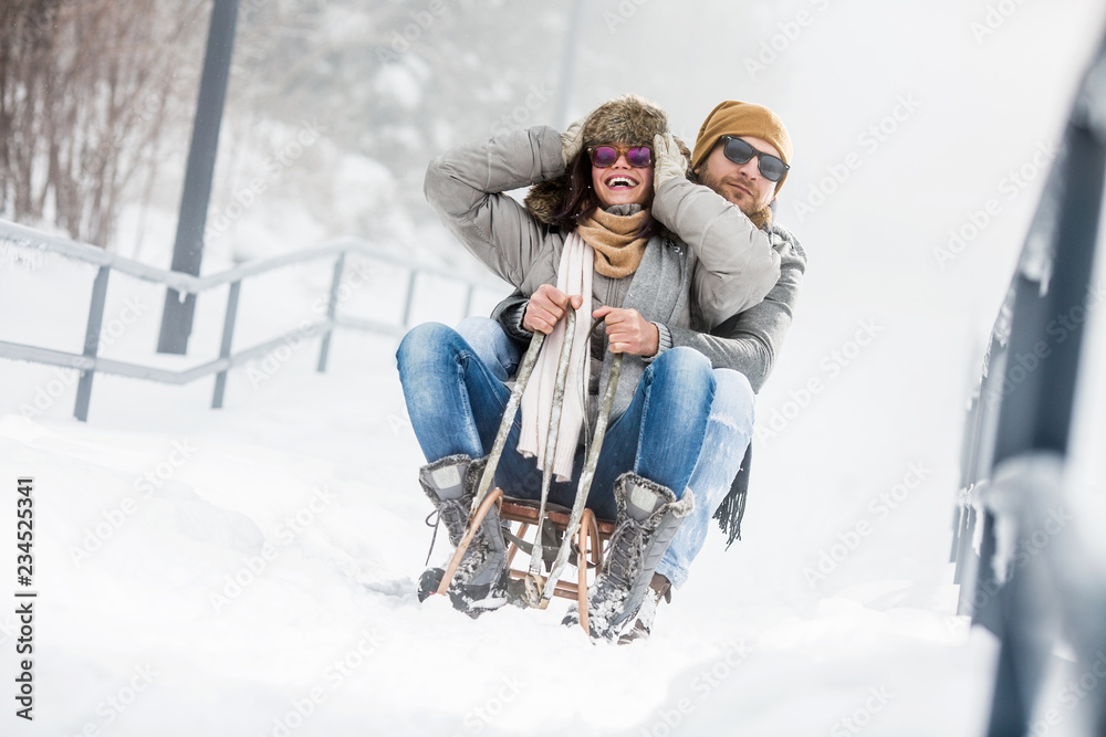 Wall mural young couple having fun with sled in snow