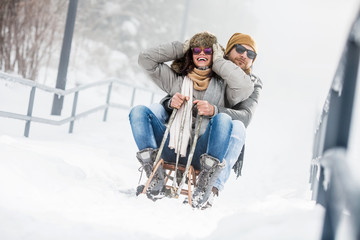 Young couple having fun with sled in snow