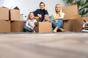 Fototapeta na wymiar Photo of parents and children among cardboard boxes in new apartment