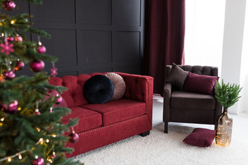 Thevelor sofa in the dark loft room has a bright light from the eternal light and an artificial fireplace. Inner attic with concrete walls and a decorated Christmas tree with gift boxes