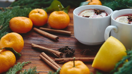 Christmas hot mulled wine in two small white cups with spices and citrus fruits on a wooden background and coniferous branches