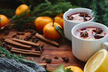  Christmas hot mulled wine in two small white cups with spices and citrus fruits on a wooden background and coniferous branches